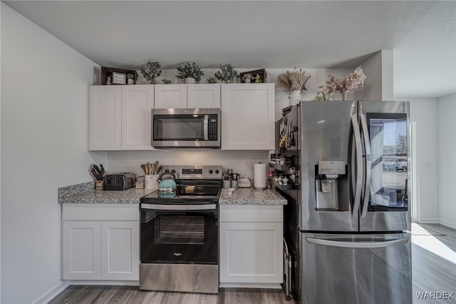 kitchen featuring white cabinets, light stone countertops, light wood-style flooring, and stainless steel appliances