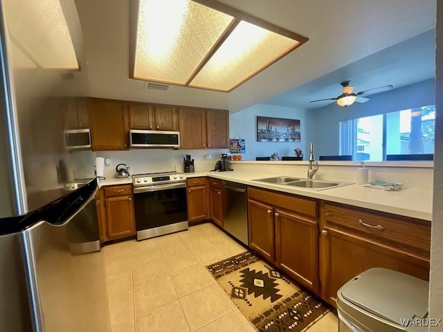 kitchen with light countertops, appliances with stainless steel finishes, a sink, and brown cabinets