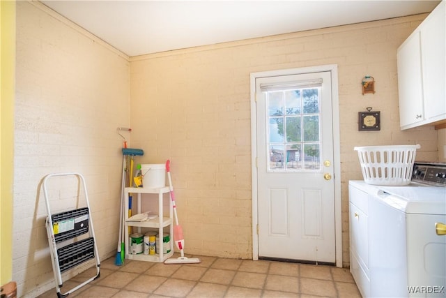 clothes washing area with cabinet space, brick wall, and independent washer and dryer