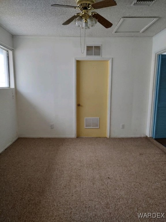 carpeted spare room featuring attic access, visible vents, a textured ceiling, and a ceiling fan