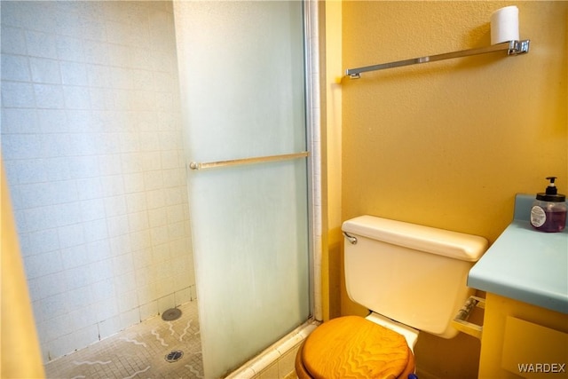 bathroom featuring tiled shower, a textured wall, vanity, and toilet