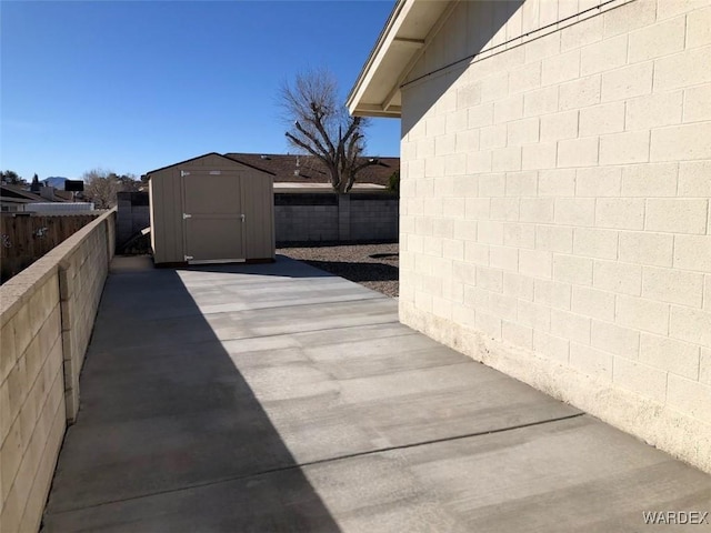 view of side of property with concrete block siding, a shed, an outdoor structure, and fence