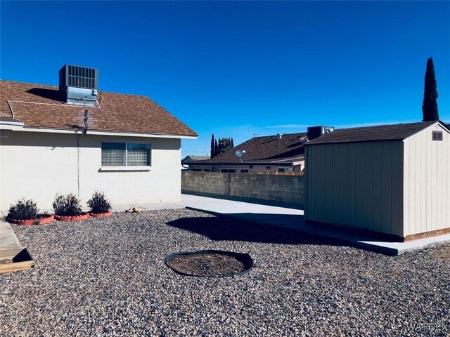 view of yard featuring an outbuilding, central air condition unit, fence, a storage unit, and a patio area