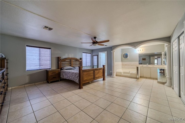 unfurnished bedroom with arched walkways, light tile patterned floors, visible vents, ceiling fan, and connected bathroom