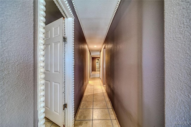 corridor with light tile patterned floors, a textured wall, and a textured ceiling