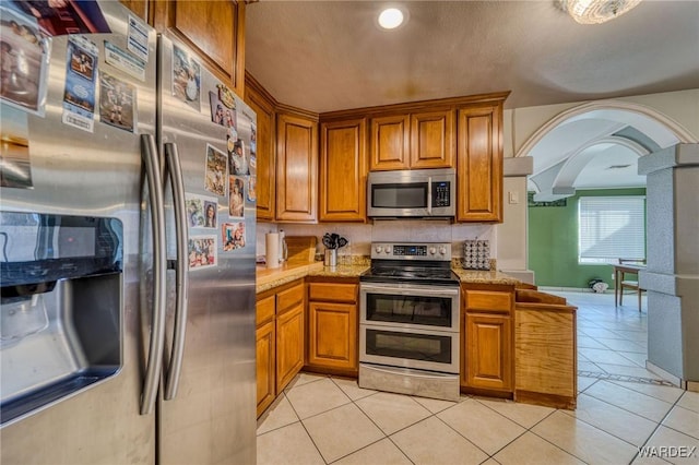 kitchen with brown cabinetry, arched walkways, stainless steel appliances, and light countertops