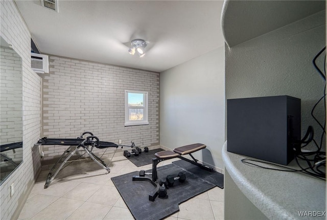 workout area with light tile patterned floors, visible vents, baseboards, brick wall, and a wall mounted air conditioner