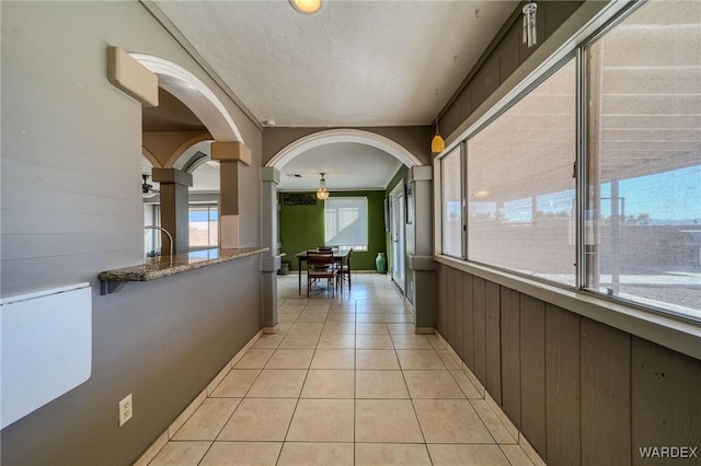 corridor with light tile patterned floors, a textured ceiling, arched walkways, and wooden walls