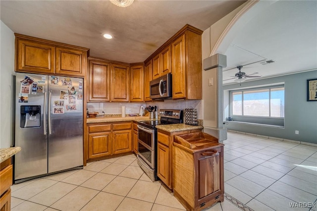 kitchen featuring light tile patterned floors, appliances with stainless steel finishes, brown cabinets, and arched walkways