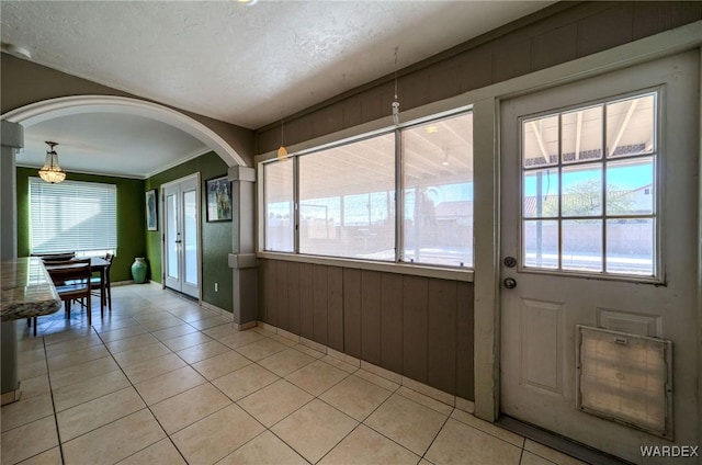 doorway to outside featuring arched walkways, a healthy amount of sunlight, a textured ceiling, and light tile patterned floors