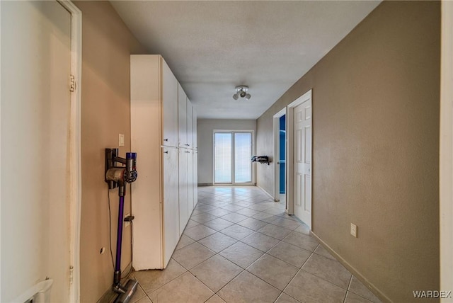 hall featuring baseboards and light tile patterned floors