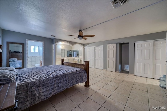 bedroom with arched walkways, visible vents, light tile patterned flooring, and two closets