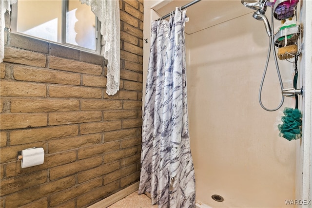 bathroom with a shower stall and brick wall