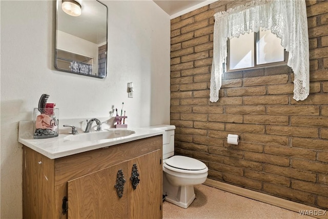 bathroom featuring toilet, brick wall, and vanity