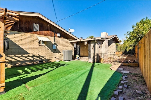 rear view of house with a yard, brick siding, a fenced backyard, and central air condition unit