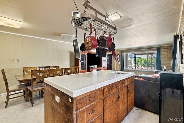 kitchen with tile counters, marble finish floor, brown cabinetry, and a sink