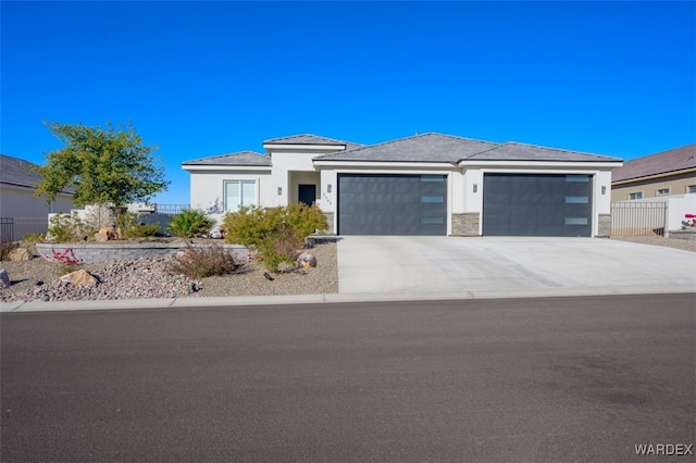 prairie-style home featuring a garage, driveway, stone siding, fence, and stucco siding