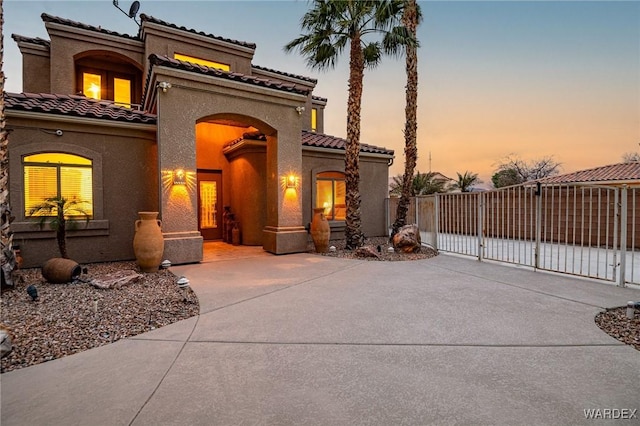 mediterranean / spanish-style house featuring a tile roof, a gate, fence, and stucco siding