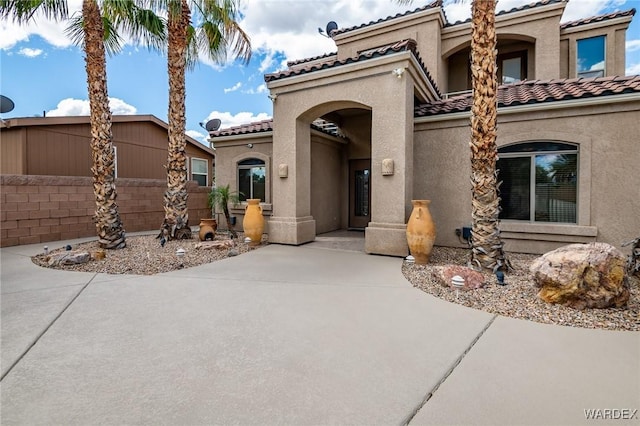 view of front of home featuring a tiled roof, a patio area, fence, and stucco siding