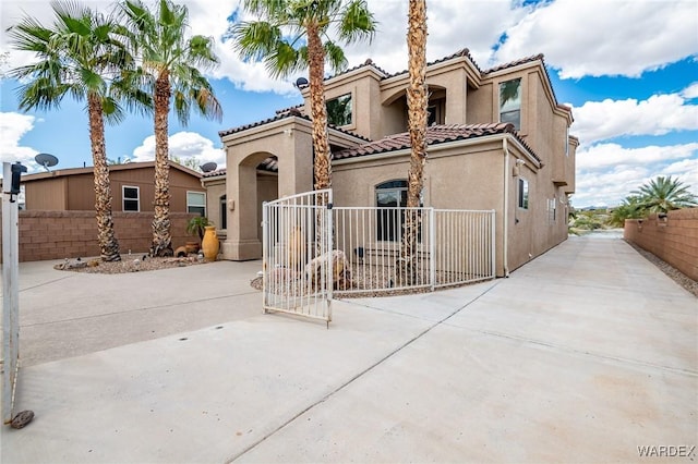 mediterranean / spanish home with driveway, a fenced front yard, a tile roof, a gate, and stucco siding