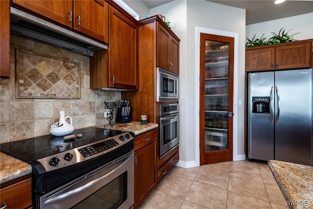 kitchen with under cabinet range hood, appliances with stainless steel finishes, decorative backsplash, and light stone counters