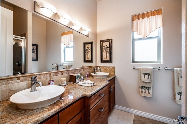 bathroom with a sink, a shower stall, baseboards, and double vanity