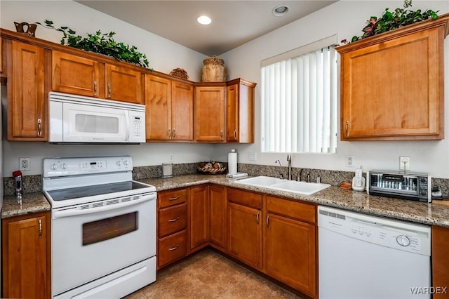 kitchen featuring white appliances, stone counters, brown cabinetry, and a sink