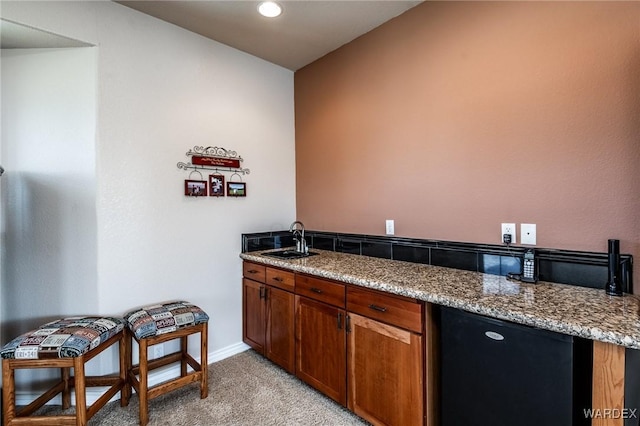 kitchen with light carpet, a sink, baseboards, light stone countertops, and brown cabinetry