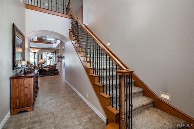 stairway featuring arched walkways, baseboards, visible vents, and a high ceiling