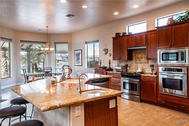 kitchen with stainless steel appliances, hanging light fixtures, a center island with sink, and tasteful backsplash