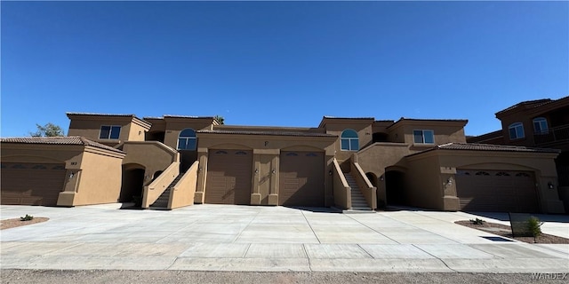 view of front facade with driveway, stairway, a tiled roof, an attached garage, and stucco siding