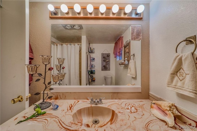 full bath with a textured wall, curtained shower, a sink, and toilet