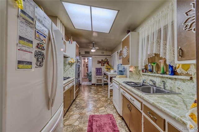 kitchen with backsplash, stone finish floor, a sink, ceiling fan, and white appliances