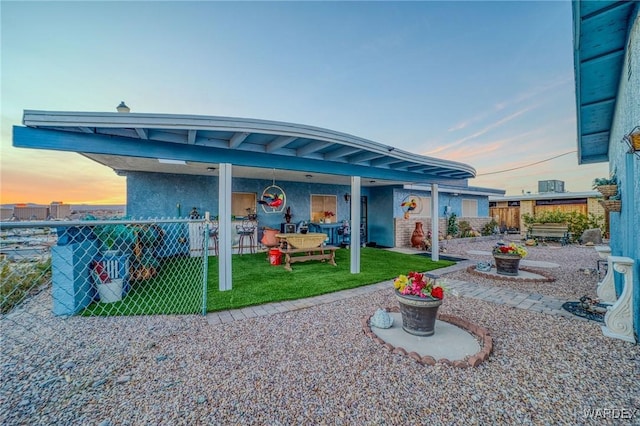 back of house at dusk featuring a patio area, fence, and stucco siding