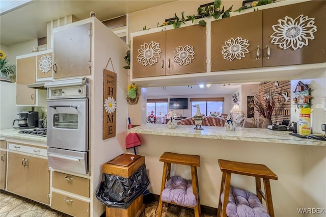 kitchen featuring a breakfast bar, a warming drawer, gas stovetop, light countertops, and stainless steel oven