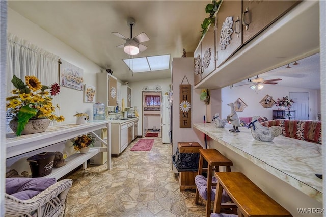 kitchen with a skylight, ceiling fan, light countertops, and freestanding refrigerator