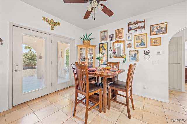 dining area featuring a ceiling fan, light tile patterned floors, baseboards, and arched walkways