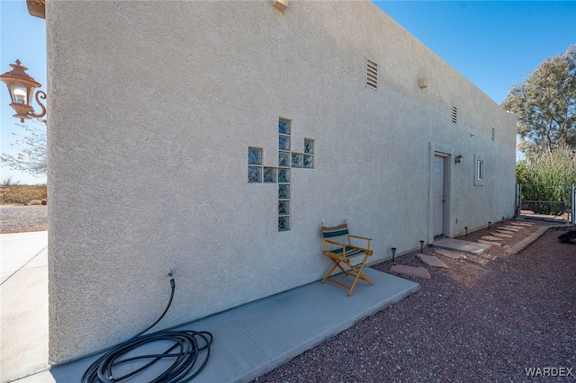 view of side of home with stucco siding and fence