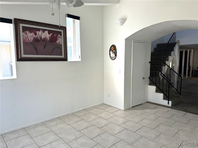 spare room with arched walkways, stairway, light tile patterned flooring, and baseboards