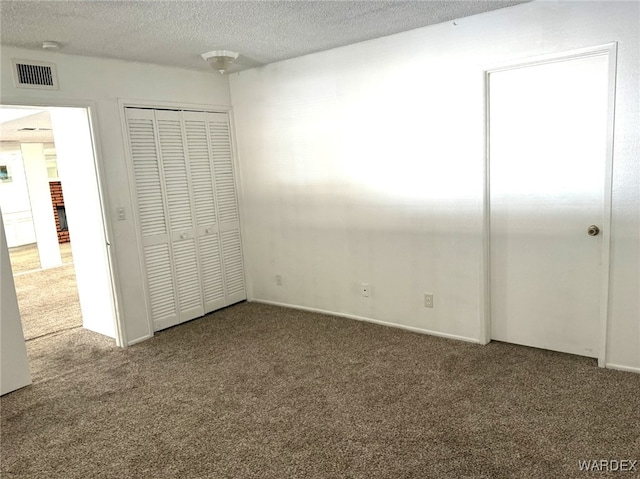 unfurnished bedroom with a textured ceiling, carpet floors, a closet, and visible vents