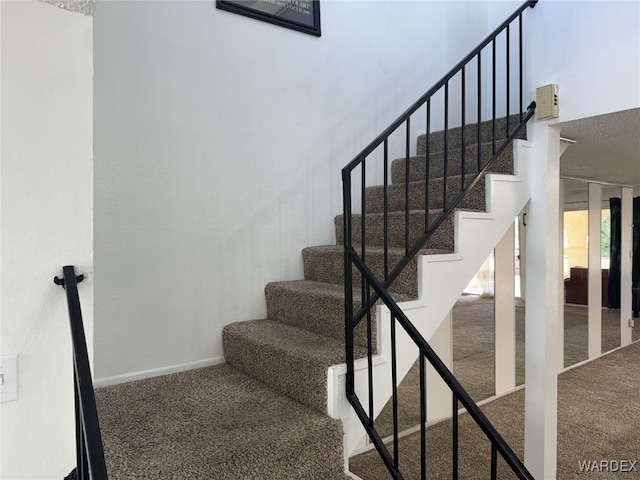 staircase with carpet, a towering ceiling, and baseboards