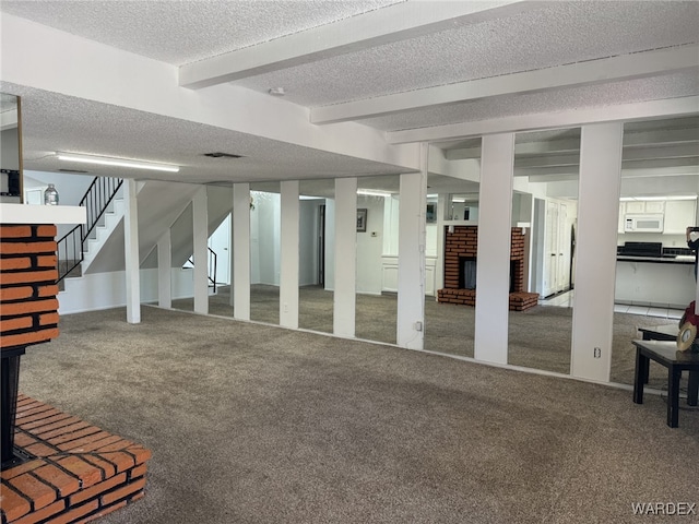 finished basement with carpet floors, a brick fireplace, stairway, and a textured ceiling