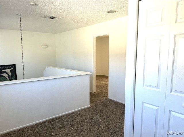 hall with a textured ceiling, dark colored carpet, visible vents, and baseboards