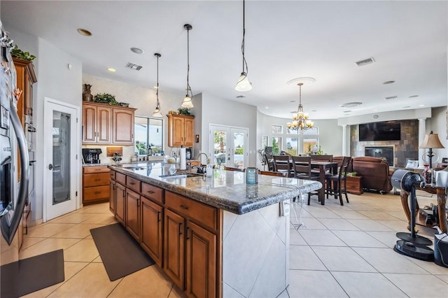 1878 E Fairway Bnd, Fort Mohave, AZ 86426 - kitchen with brown cabinetry, an island with sink, hanging light fixtures, dark stone counters, and light tile patterned floors
