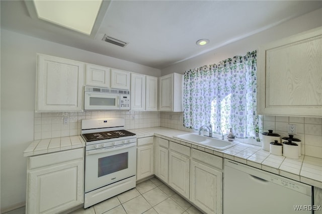 kitchen featuring visible vents, white appliances, tile counters, and a sink