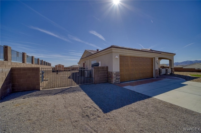 view of side of property featuring driveway, a garage, stone siding, a gate, and stucco siding