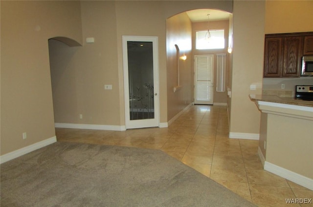 interior space with arched walkways, decorative light fixtures, light tile patterned floors, appliances with stainless steel finishes, and baseboards