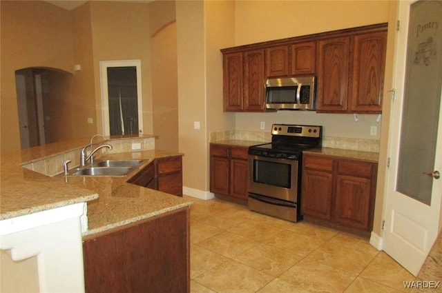 kitchen with arched walkways, a peninsula, appliances with stainless steel finishes, and a sink