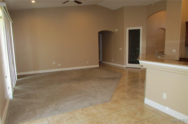 spare room featuring arched walkways, light tile patterned floors, lofted ceiling, and a ceiling fan