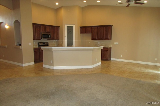 kitchen with arched walkways, a center island with sink, light countertops, appliances with stainless steel finishes, and high vaulted ceiling